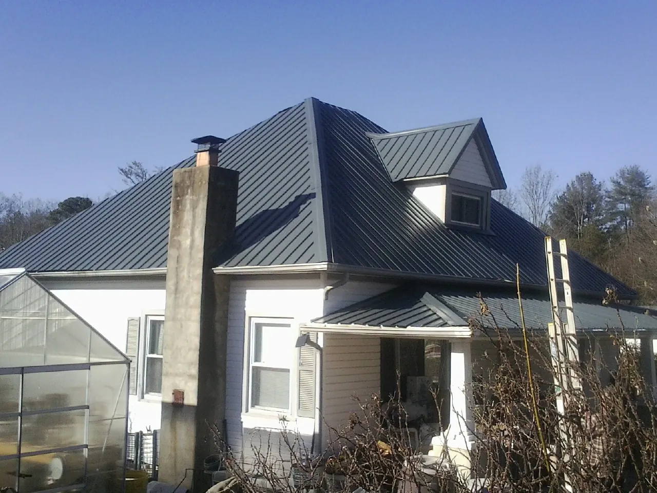 Dark blue standing seam metal roof on a white farmhouse with dormer — Slate & Tile Roof Repair by Roofing Brothers in Penn Run
