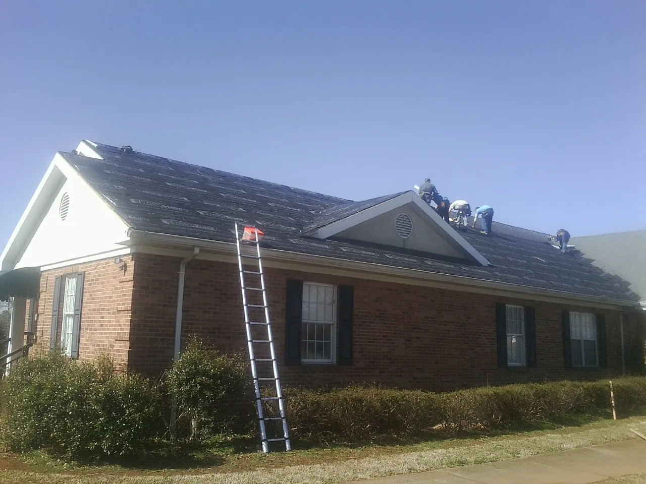 Crew tearing shingles off a brick ranch roof with a ladder set — Metal Roof Repair work by our crew in Penn Run