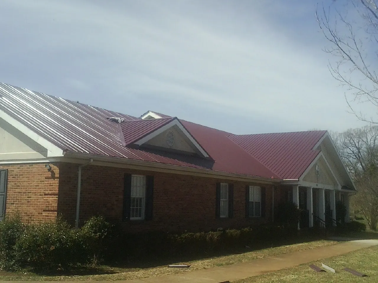 Red metal roof with gabled entries on a long brick building, from a Hail Damage Roof Repair job in Penn Run