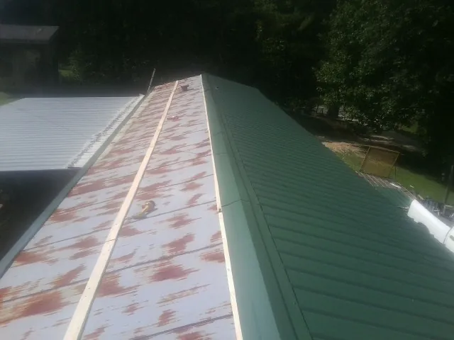 Old rusted panels beside newly installed green metal roofing — Wind Damage Roof Repair by Roofing Brothers in Penn Run