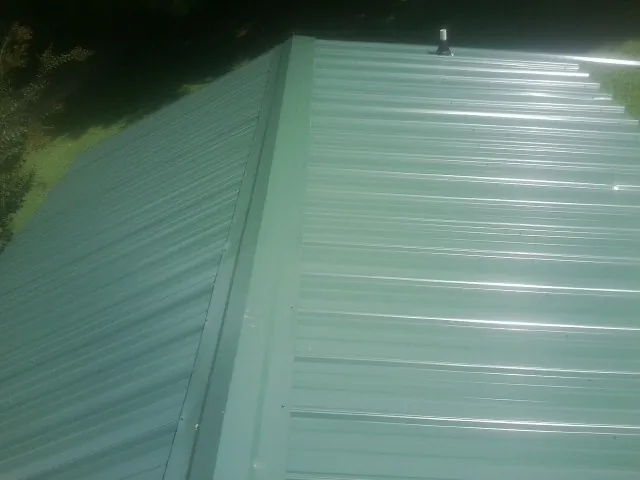 New green metal panels meeting at the ridge of a roof — Flat Roof Repair work by our crew in Penn Run