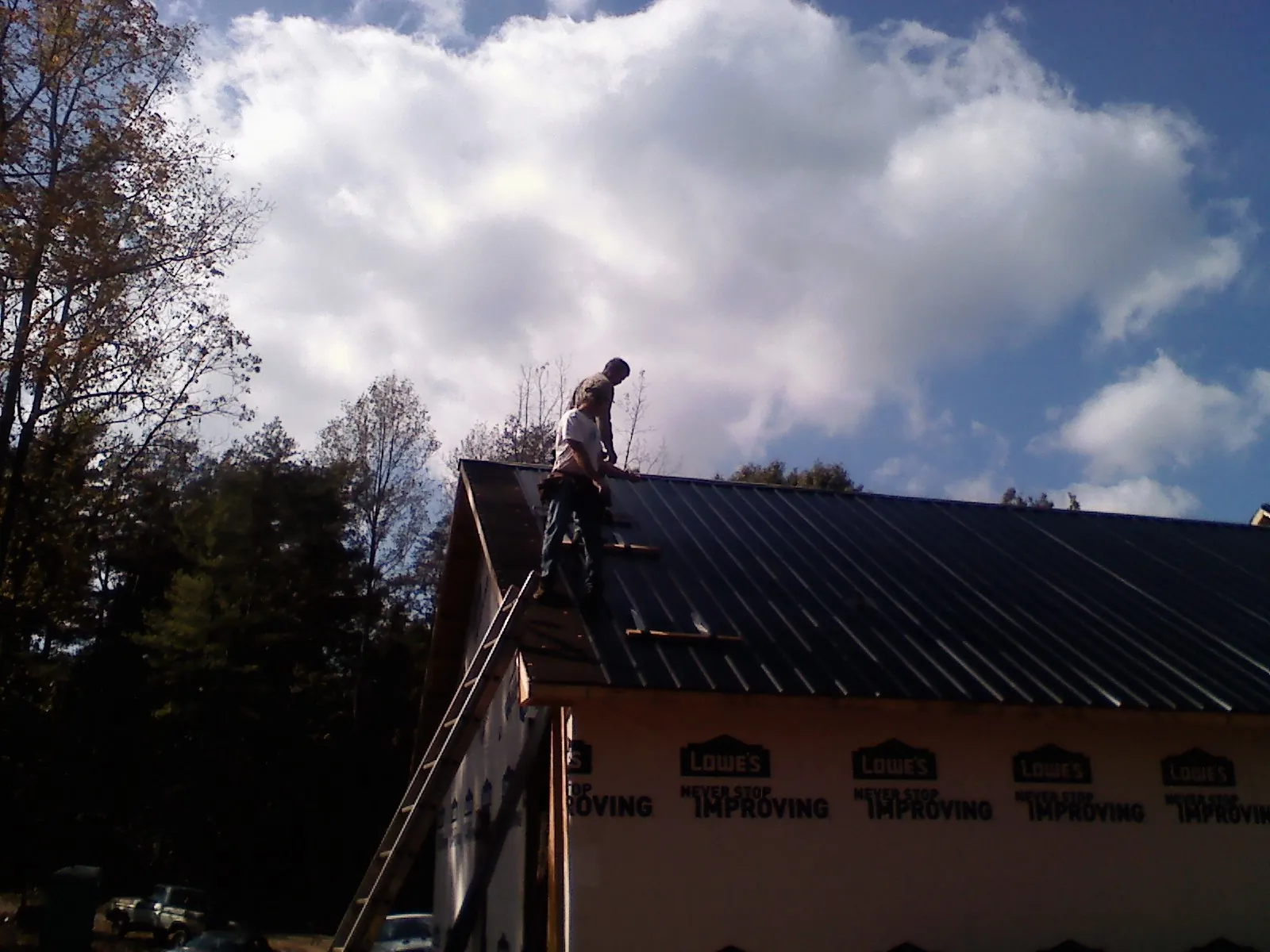 Roofer fastening dark metal panels high against a cloudy sky, from a Roof Inspection job in Penn Run