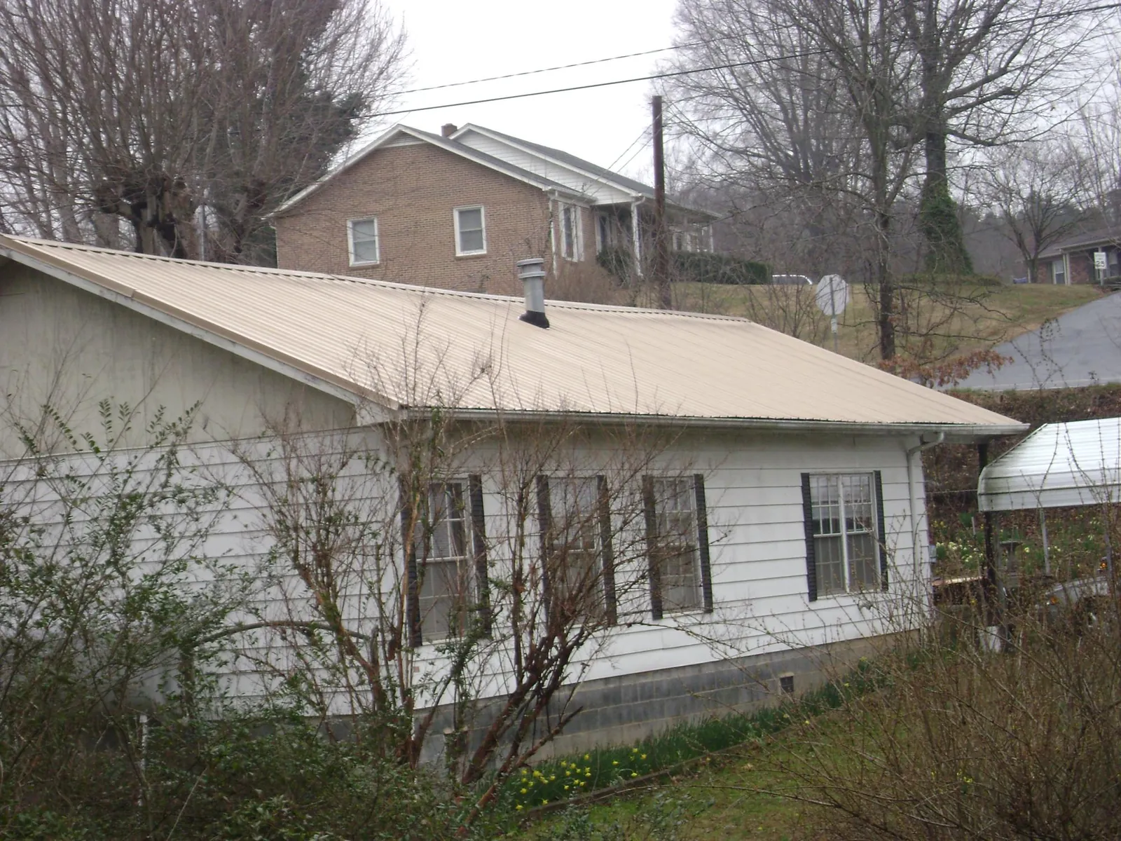Tan metal roof on a white sided house set into a hillside — Commercial Roofing by Roofing Brothers in Penn Run